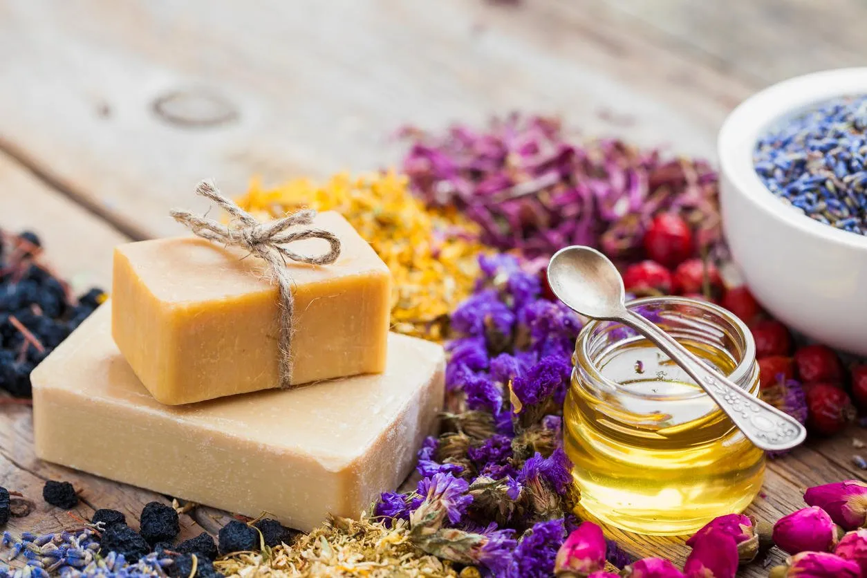 bars of homemade soaps, honey or oil, heaps of healing herbs and mortar of lavender selective focus