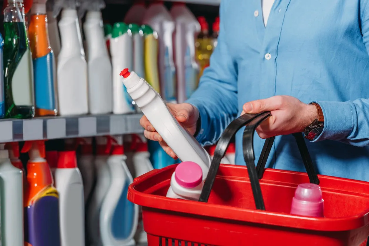 partial view of shopper putting detergent into shopping basket in supermarket
