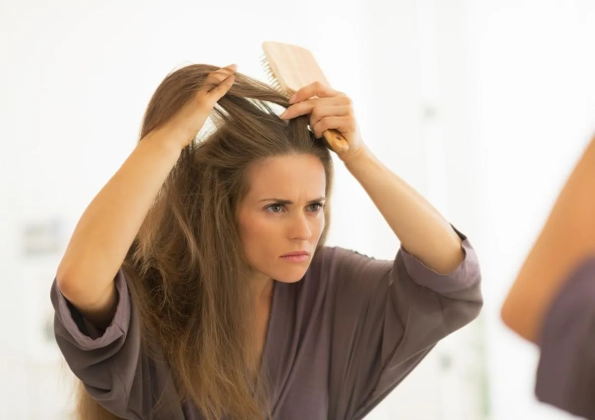 concerned young woman combing hair in bathroom