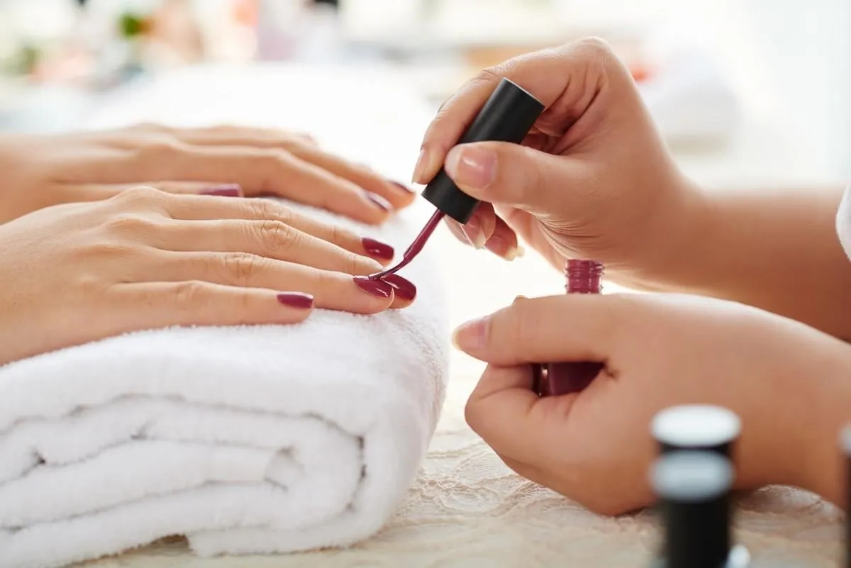 side view of manicurist applying marsala nail polish