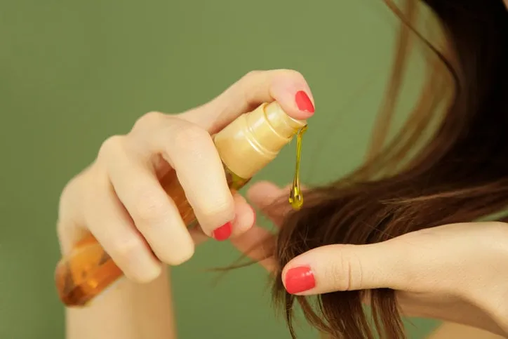 woman applying oil on hair ends, split hair tips, dry hair or sun protection concept