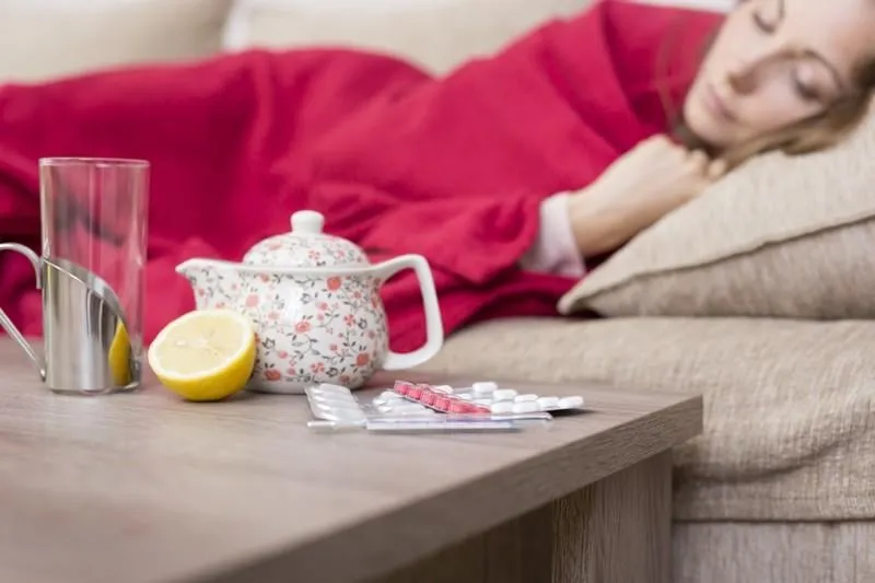 femme malade recouverte d'une couverture couchée dans son lit avec une forte fièvre et des pilules contre la grippe, théière et citron sur la table mise au point sélective sur les pilules