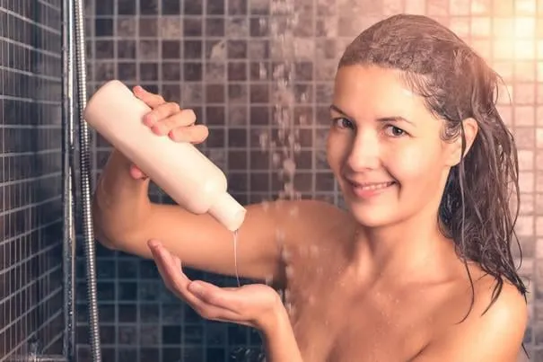 gros plan de jeune femme nue prenant une douche à la salle de bain, verser le gel de bain sur sa main tout en souriant à la caméra