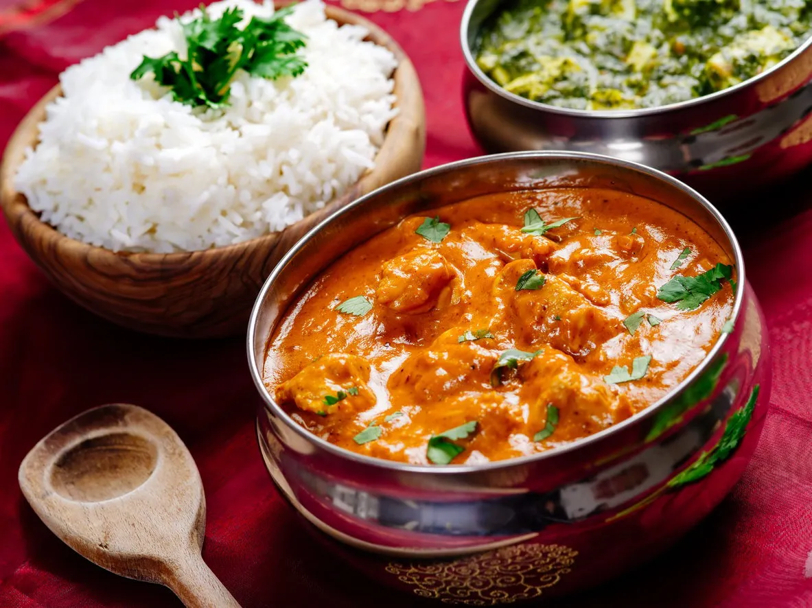 photo of an indian meal of butter chicken, rice and saag paneer focus across the butter chicken bowl