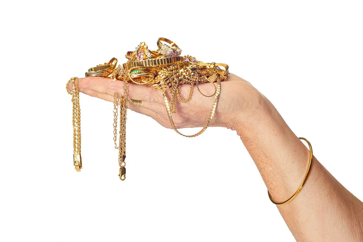 horizontal shot of a womanu2019s hand holding a pile of gold jewelry some of which is hanging down from her hand she is also wearing a bracelet isolated on white copy space