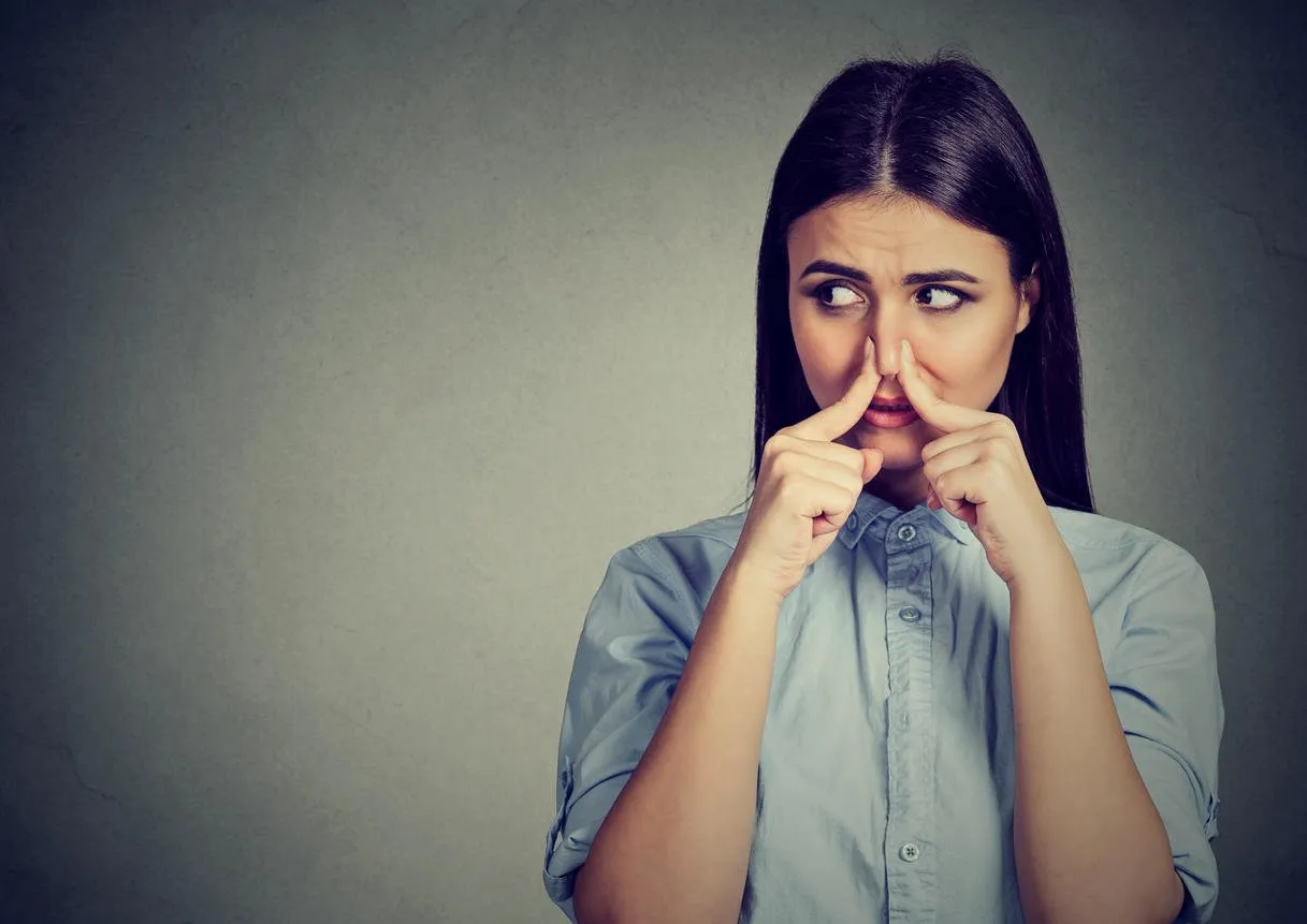 woman pinches nose with fingers looks with disgust away something stinks bad smell isolated on gray background