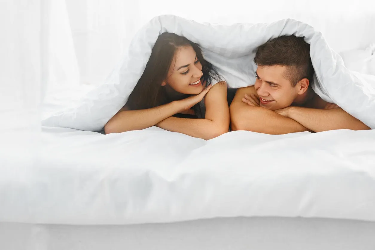 young beautiful couple having fun lying on the bed under the blanket in the morning relationship concept