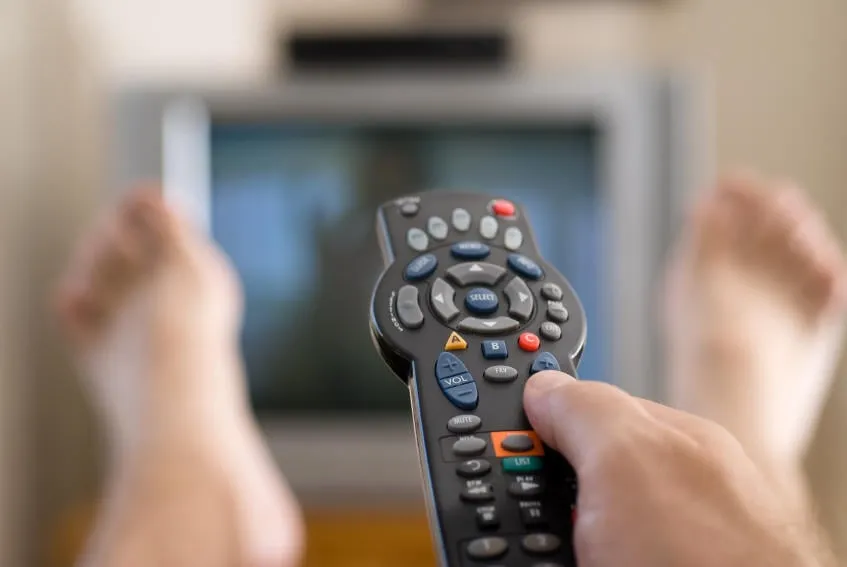 un homme regarde la télévision et change de chaîne tout en se relaxant un dimanche après-midi