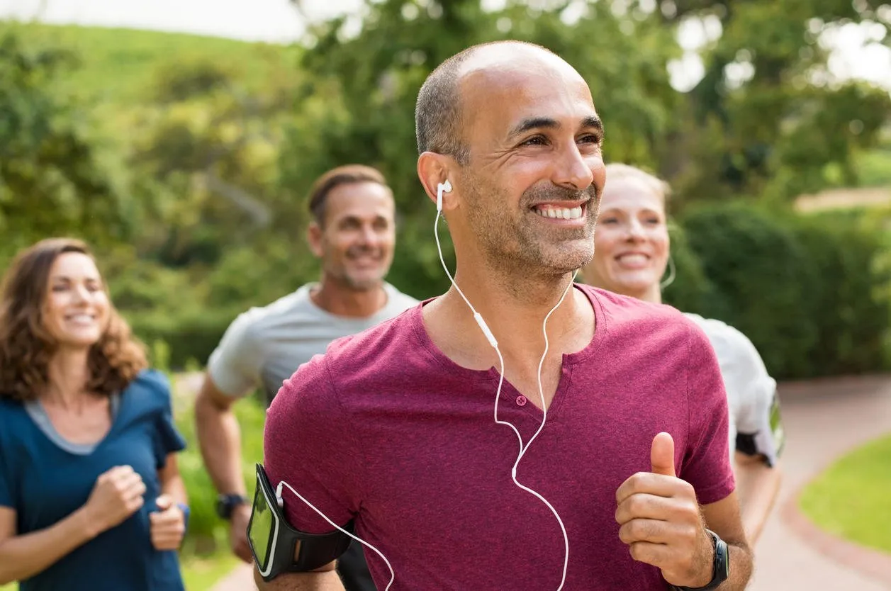 portrait of a happy cheerful man listening to music while jogging man listening to music while jogging with group happy trainer in park running with teamr