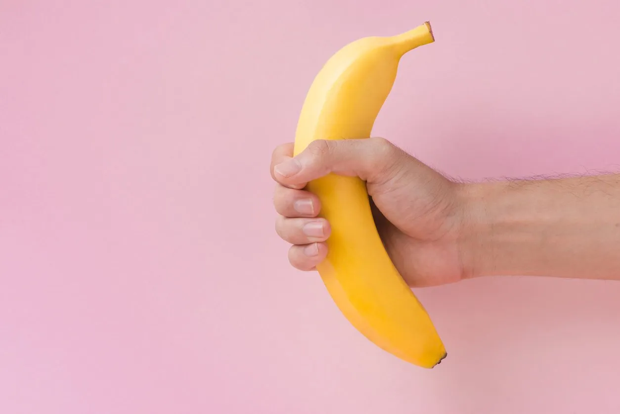 male hand holding a banana isolated on pink background