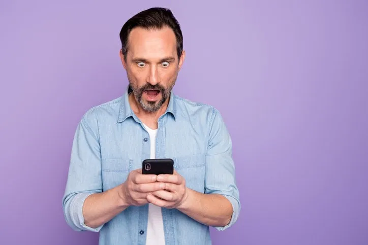 portrait of amazed shocked man use cellphone read social network, information stare stupor scream wow omg wear good looking clothing isolated over violet color background