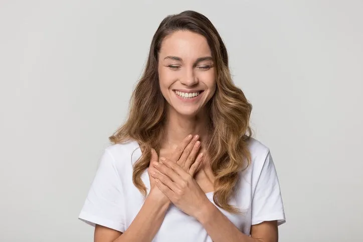 happy pleased young woman thanking for care feel grateful holding hands on chest to heart isolated on white studio blank background, smiling sincere girl showing love heartfelt gratitude appreciation