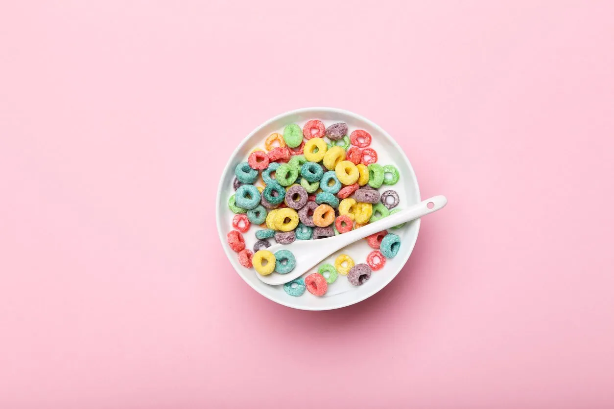 colorful corn rings in bowl with milk and spoon on pink background
