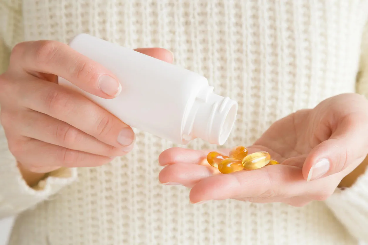 woman spilling out fish oil capsules from bottle in her hand receiving vitamins women's issues nutritional supplements and healthcare concept