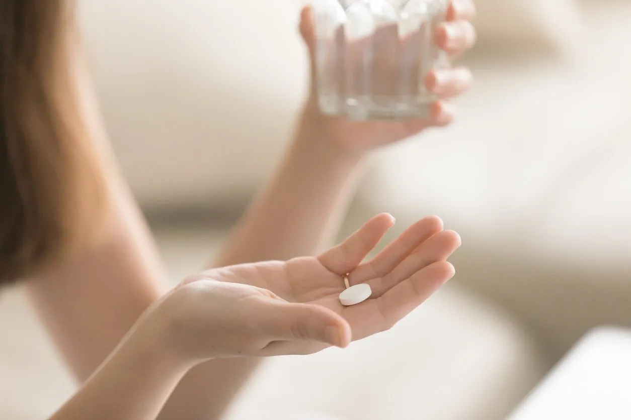 close up photo of one round white pill in young female hand woman takes medicines with glass of water daily norm of vitamins, effective drugs, modern pharmacy for body and mental health concept