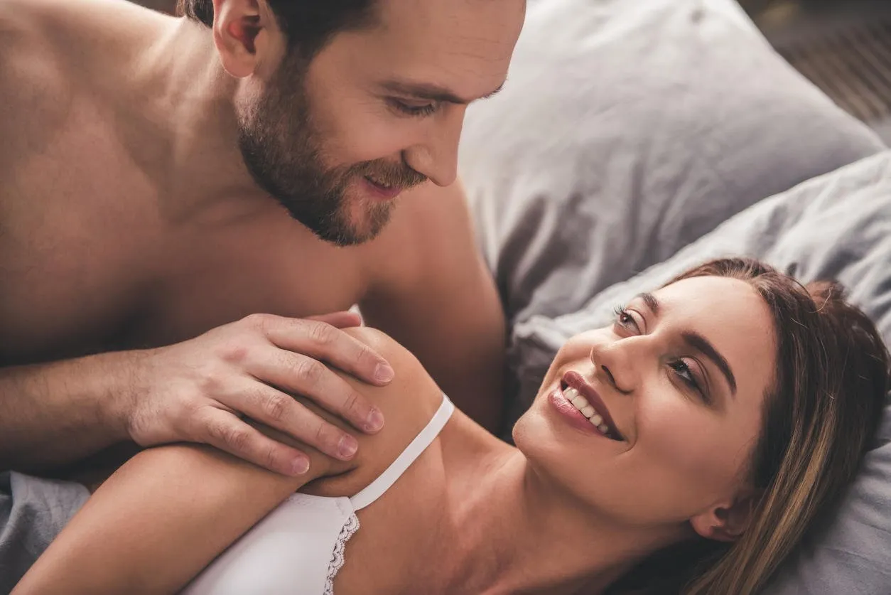beautiful couple is looking at each other and smiling while lying together in bed at home