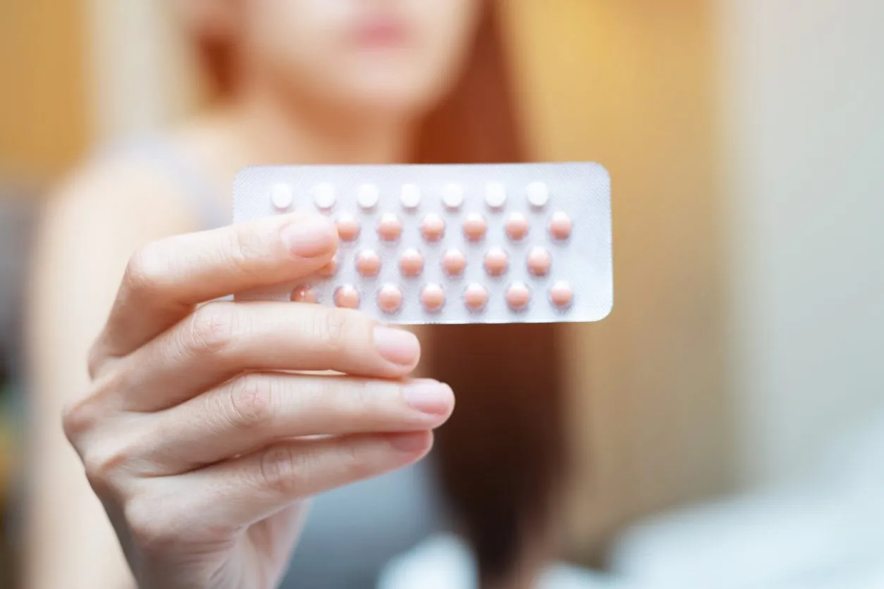 woman hands opening birth control pills in hand on the bed in the bedroom eating contraceptive pill