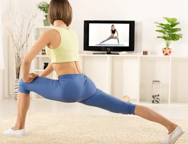 jeune femme en tenue de sport, athlétique, photographié par derrière, exercice dans la salle, devant la télé