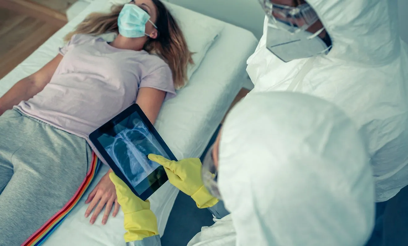 doctors with bacteriological protective suits examining a patient's chest x-ray