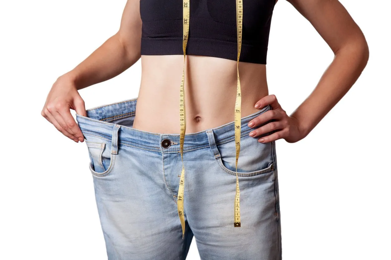 close-up of slim waist of young woman in big jeans showing successful weight loss, isolated on white background, diet concept