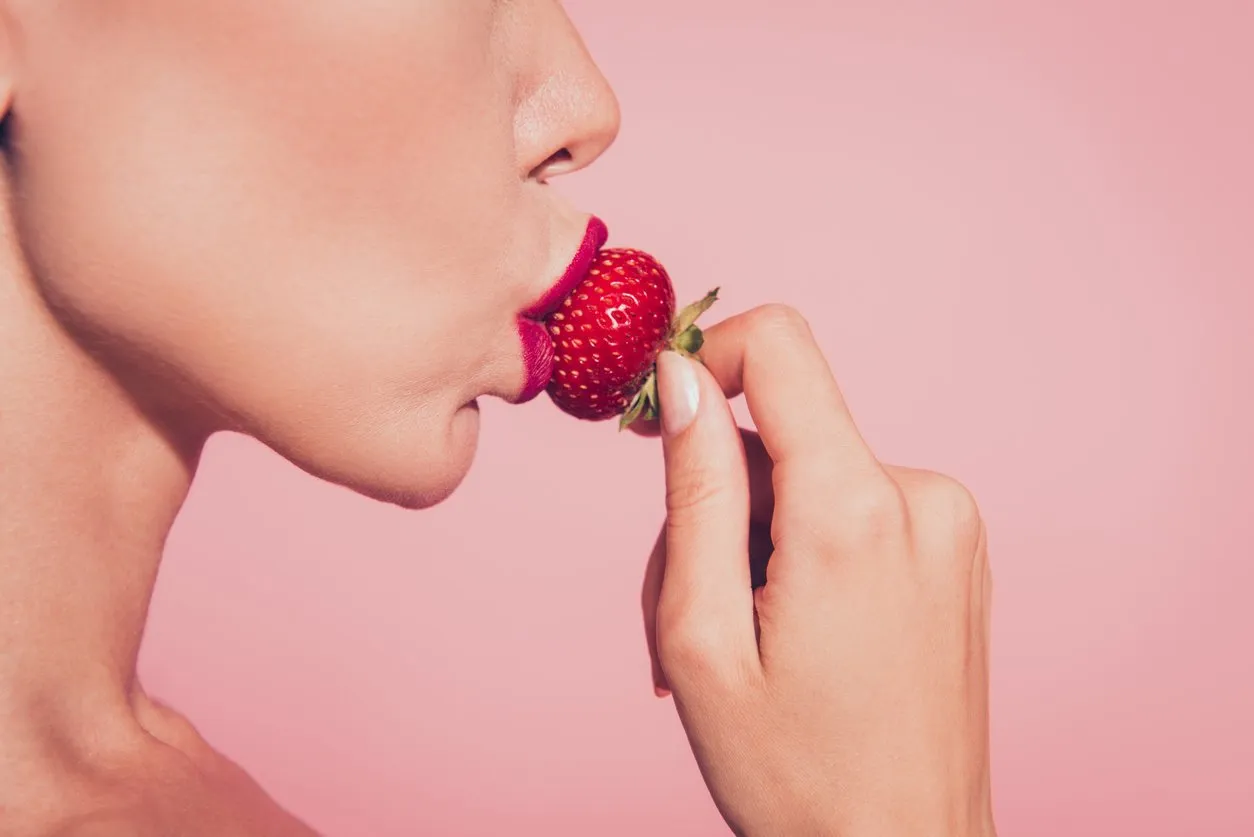 close-up cropped half face profile side view portrait of lovely sweet luxurious feminine glamorous wavy-haired lady eating biting licking tasting enjoying dessert red lips isolated on pink background