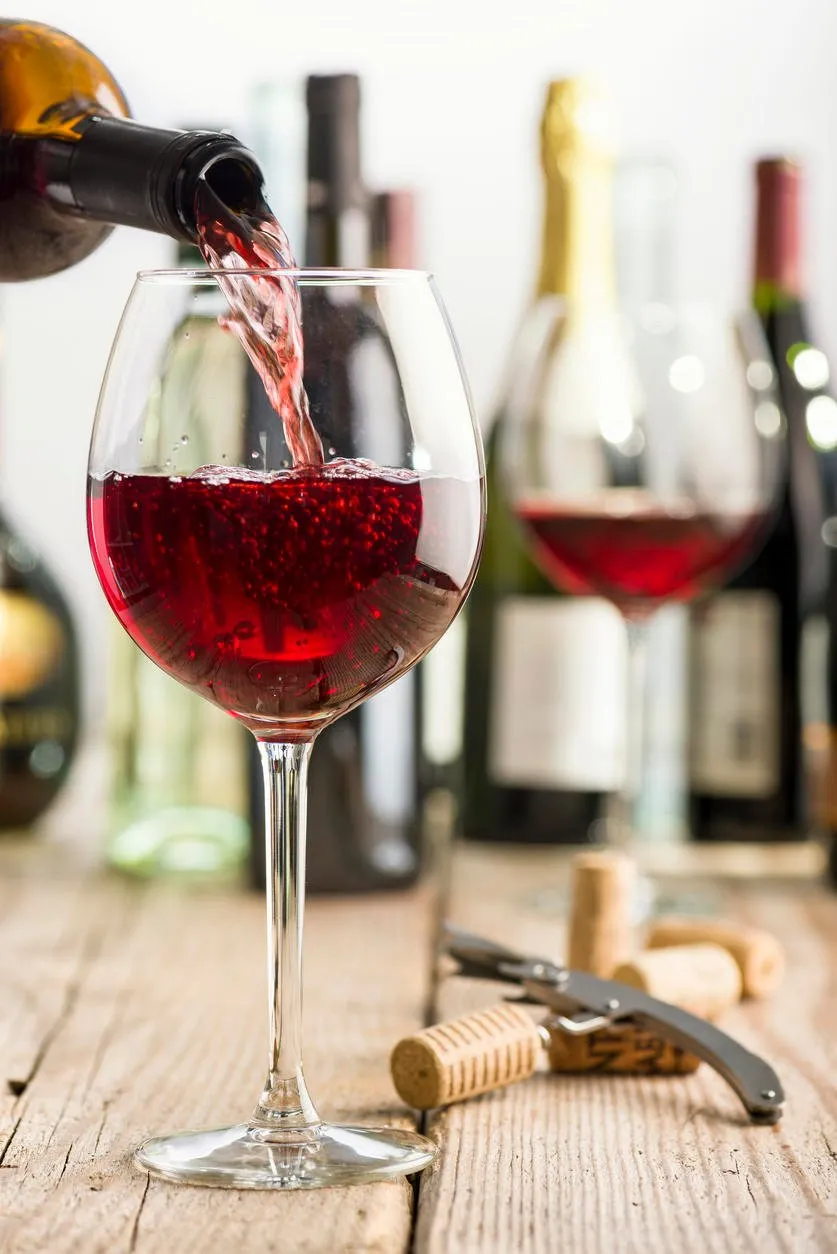 verser le vin rouge en verre sur une table en bois près de tire-bouchon et bouteille