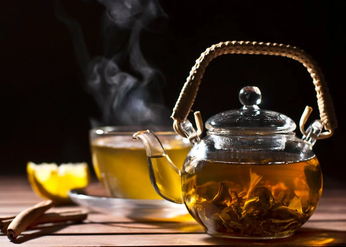 thé vert en verre théière sur la table en bois sur le fond à la vapeur tasse de thé, morceau de citron et de bâtons de cannelle