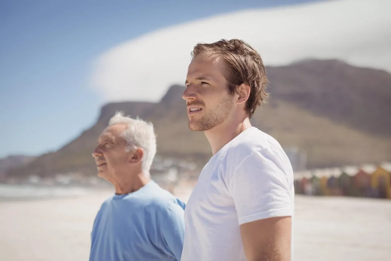young man with his father standing at beach during sunny day