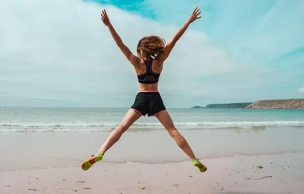 une jeune femme fait des sauts étoiles sur la plage au bord de la mer