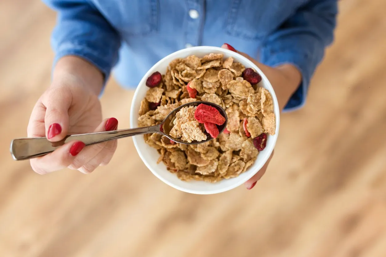 close-up of hands of young woman holding bowl with breakfast cereals at home