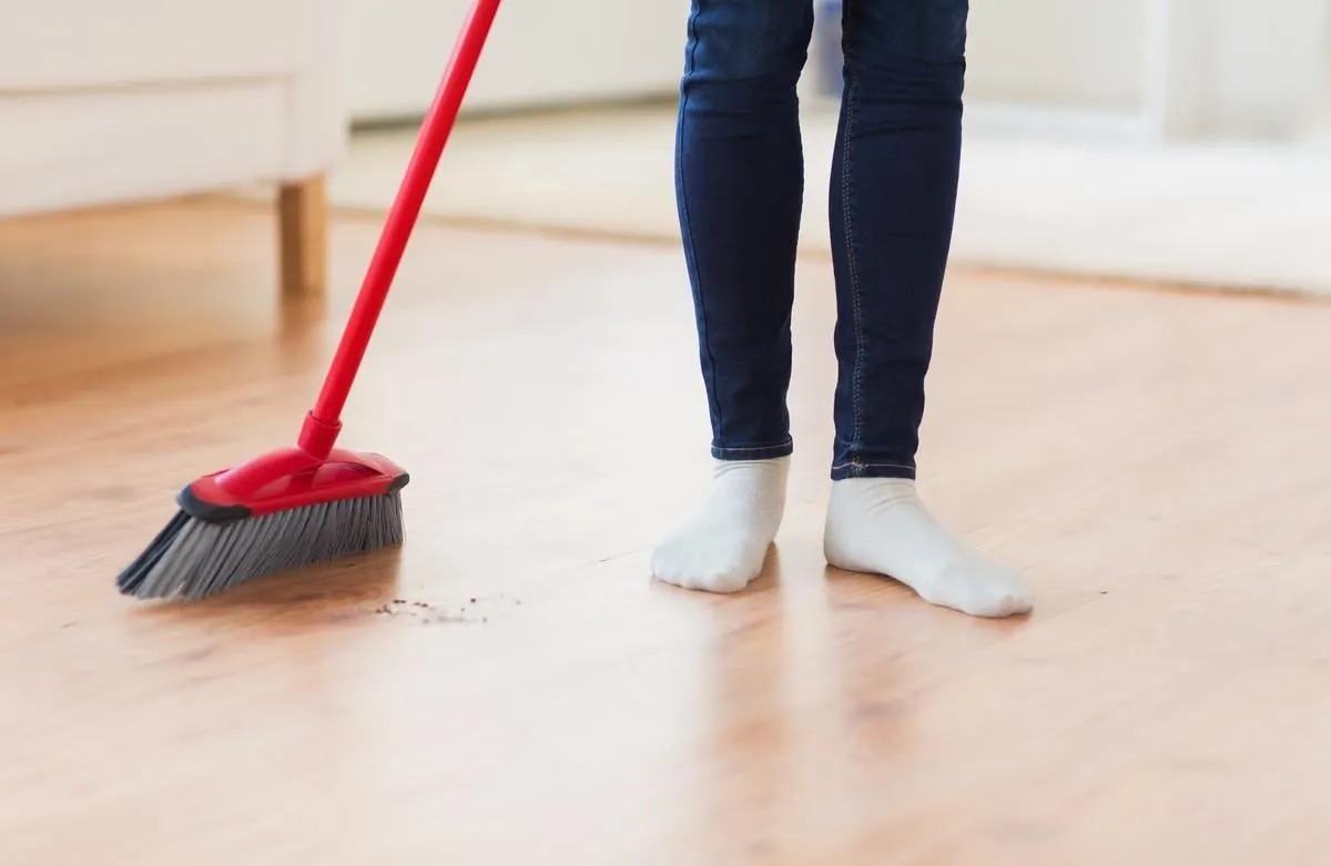 people, housework, cleaning and housekeeping concept - close up of woman legs with broom sweeping floor at home