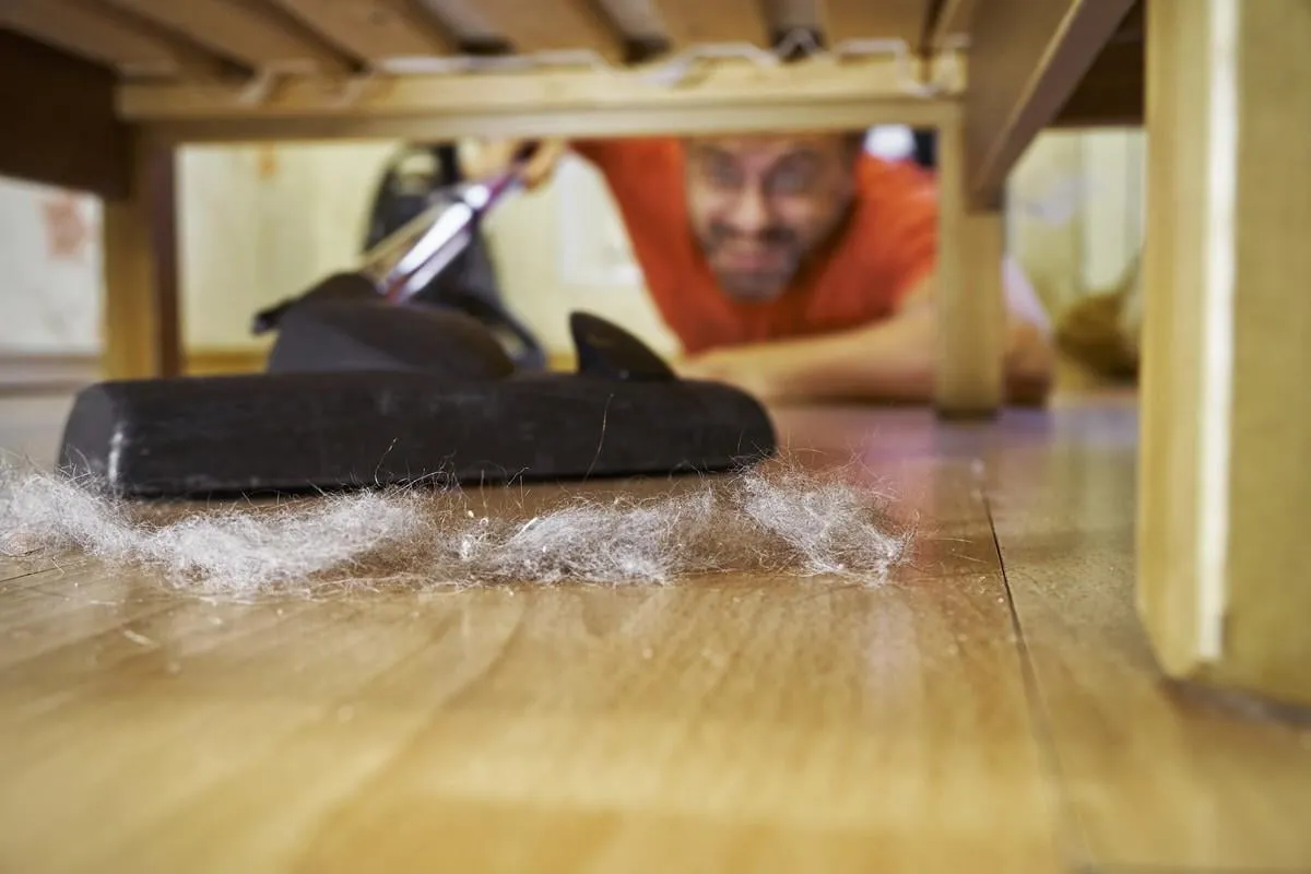 man cleaning a floor under a bed with vacuum cleaner