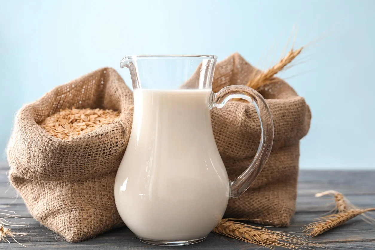 pitcher of milk and bags with oatmeal flakes on light background