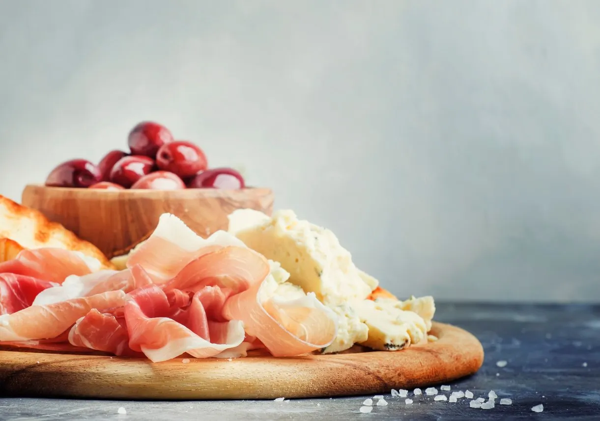snacks or antipasti, crostini, prosciutto, blue cheese and olives, gray background, selective focus
