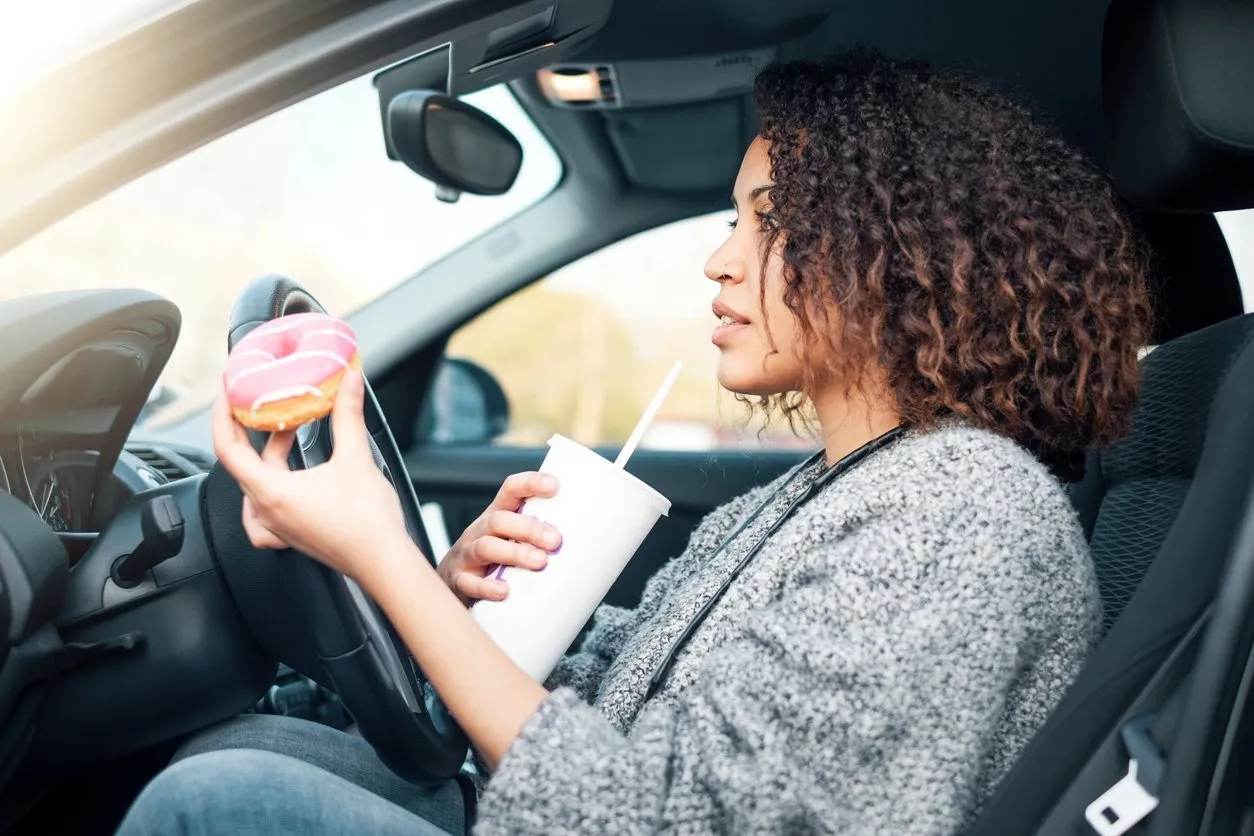 woman eating a sweet and drinking driving her car