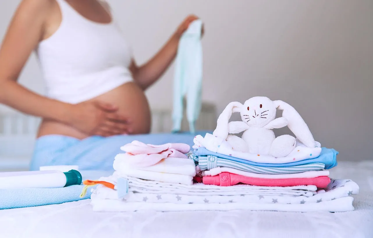 pile of baby clothes, necessities and pregnant woman on bed in home interior of bedroom pregnant woman is getting ready for the maternity hospital, packing baby stuff pregnancy, birth concept