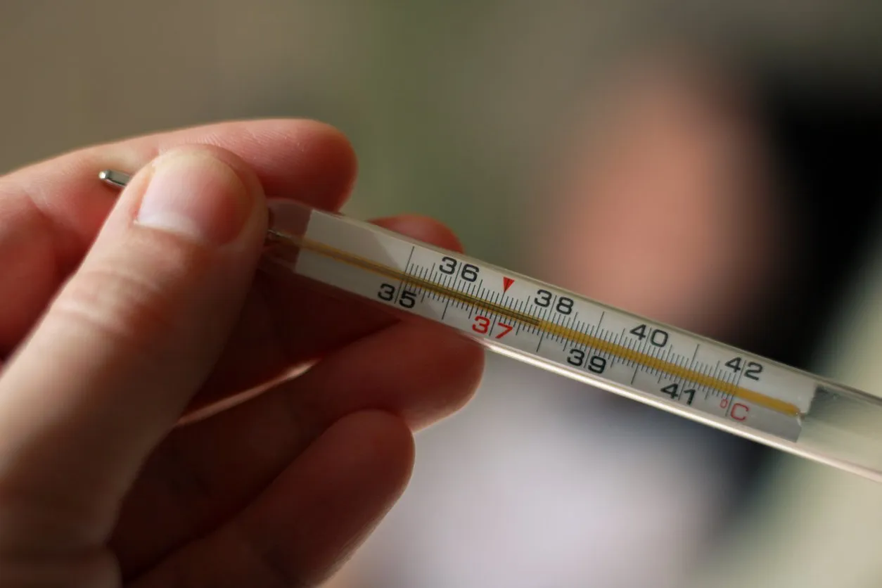 an alcohol thermometer shows a temperature of 379 on a blurred background of a sick girl lying on a bed check the temperature fever, illness, chills, care