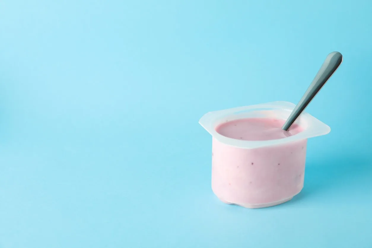 plastic cup with yogurt and spoon on color background, space for text