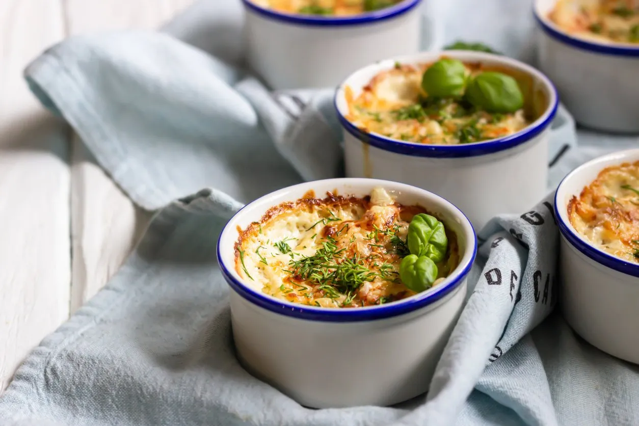 hot appetizer (julien) with champignons, chicken fillet, cheese and basil in porcelain ceramic forms close up, selective focus