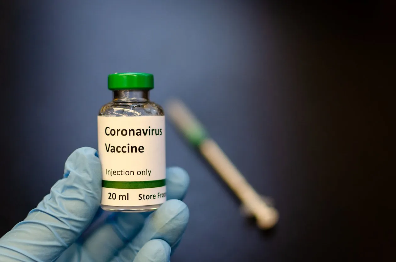 doctor holding coronavirus vaccine vial with syringe at the background