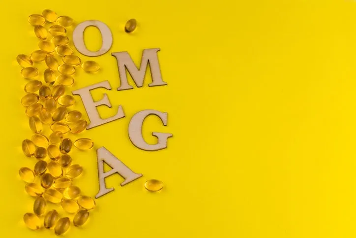 the inscription omega made of wooden beech and fish oil capsules on a yellow background copy space