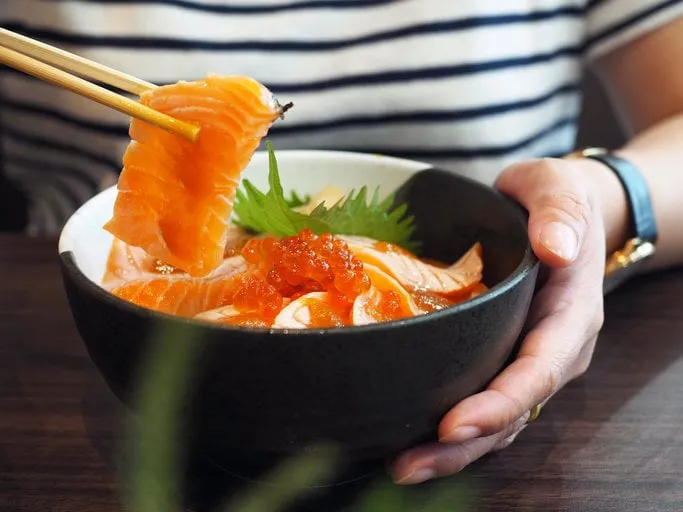 bowl of sliced grilled salmon or aburi sashimi top with salmon roe served with wasabi, pickled ginger, seaweed and oba leaf and bowl of mixed salad japanese traditional food with selective focus