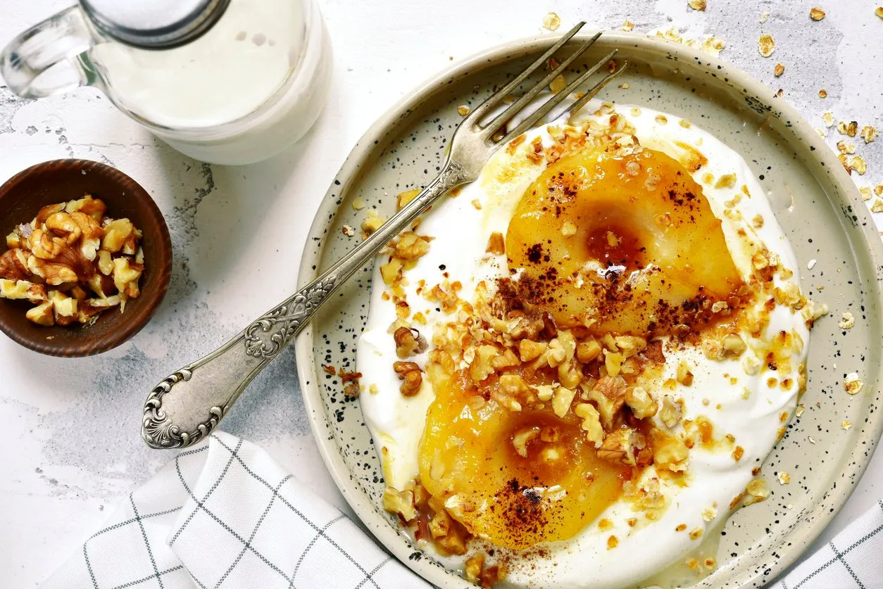 caramelized pear with nuts and yogurt for a breakfast on a rustic craft plate over white slate,stone or concrete backgroundtop view