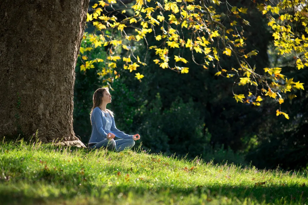 girl meditates sitting on the grass under a maple tree in autumn