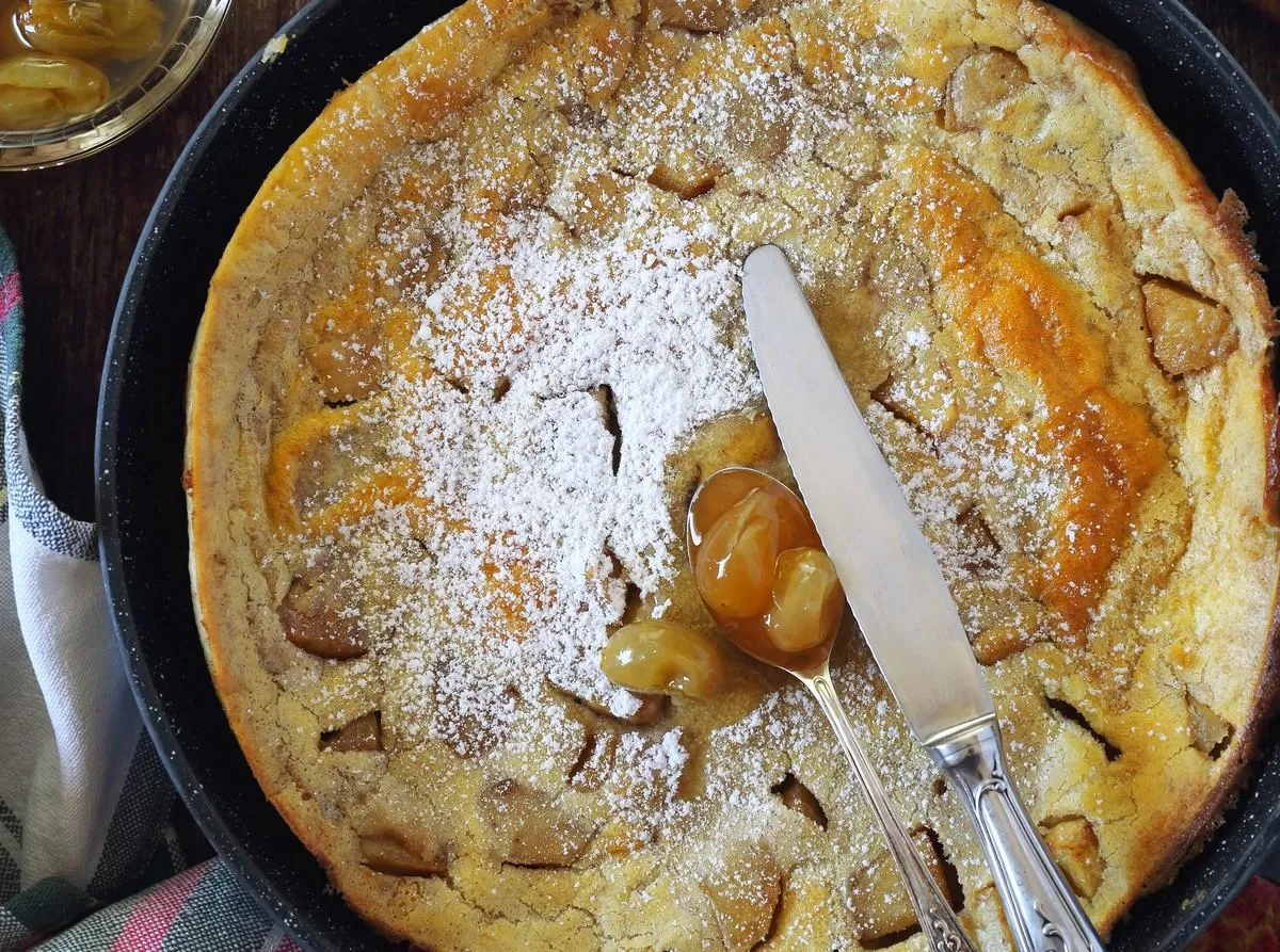 american cuisine  apple dutch baby lush omelet in frying pan, powdered sugar and green grapes jam dressing top view, rustuc style