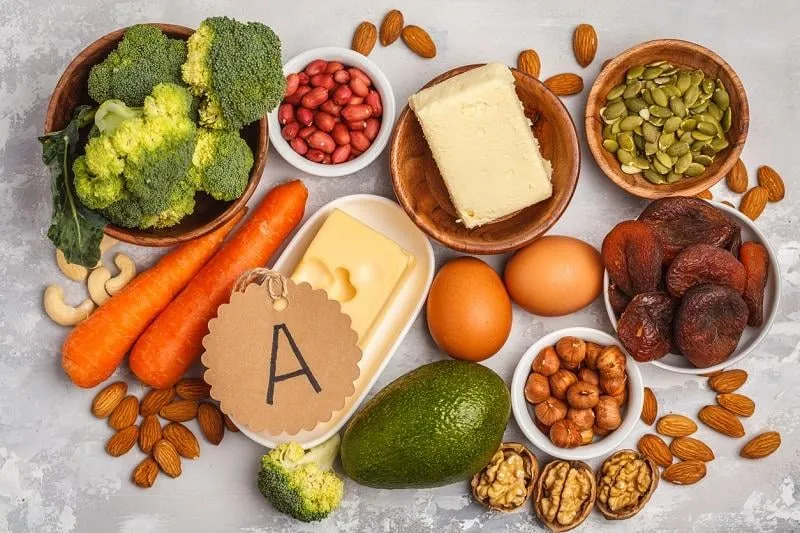 healthy food nutrition dieting concept assortment of high vitamin a sources carrots, nuts, broccoli, butter, cheese, avocado, apricots, seeds, eggs white background, top view