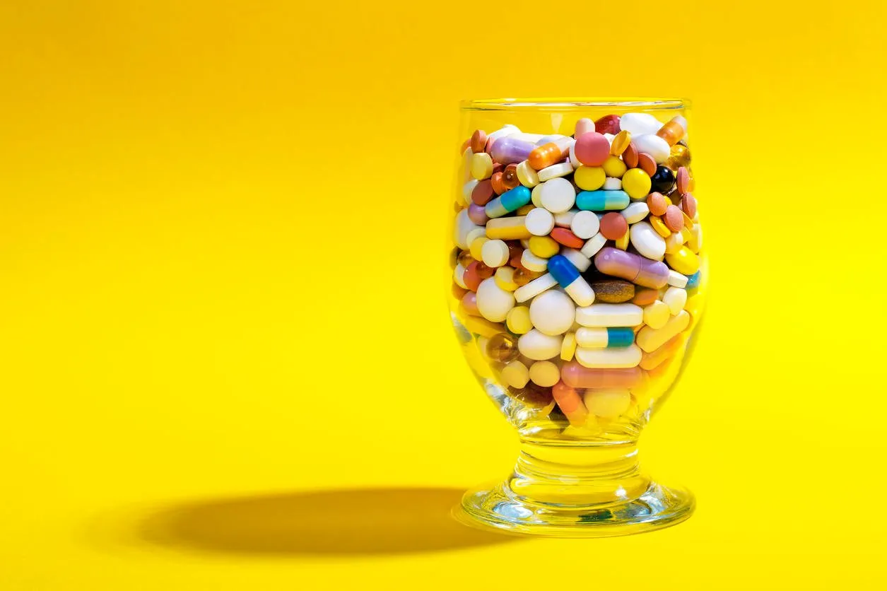 glass full of colorful pills on a yellow background creative composition