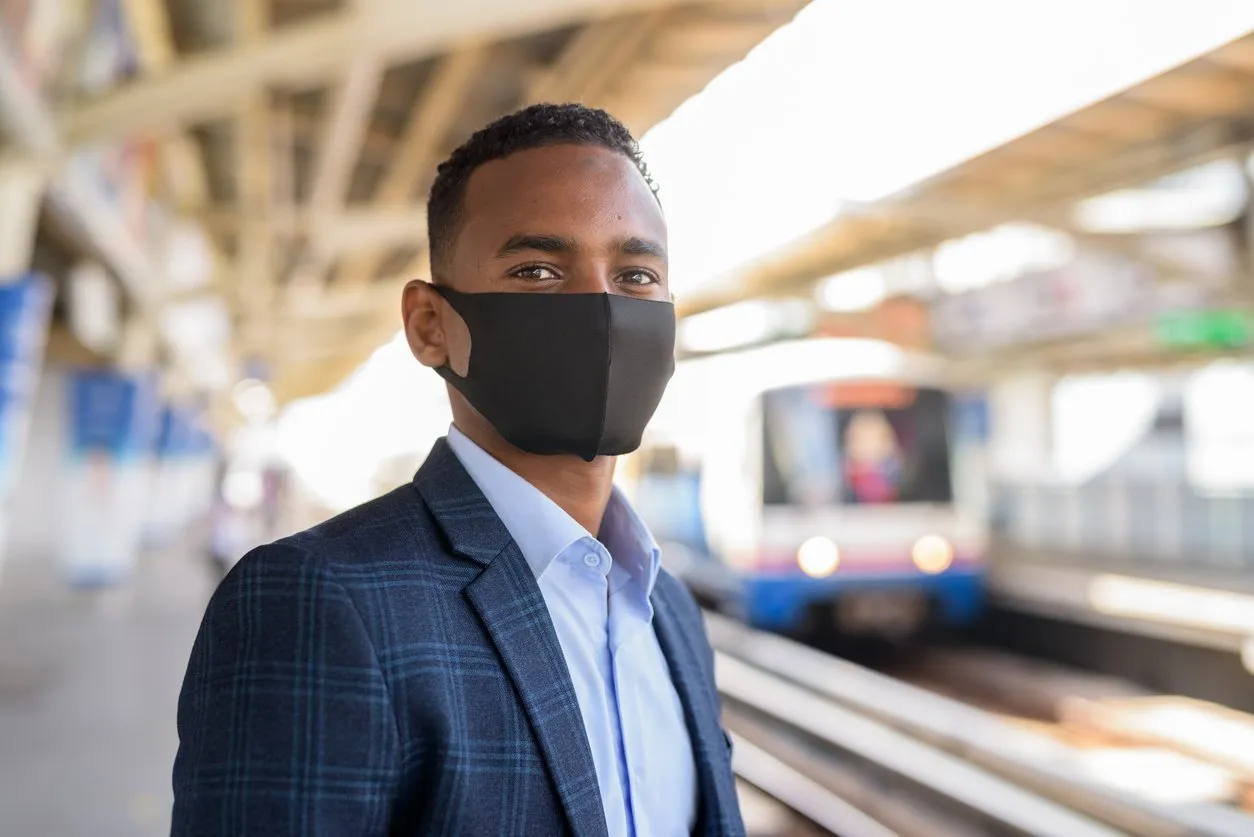 young african businessman with mask for protection from corona virus outbreak thinking and waiting at sky train station