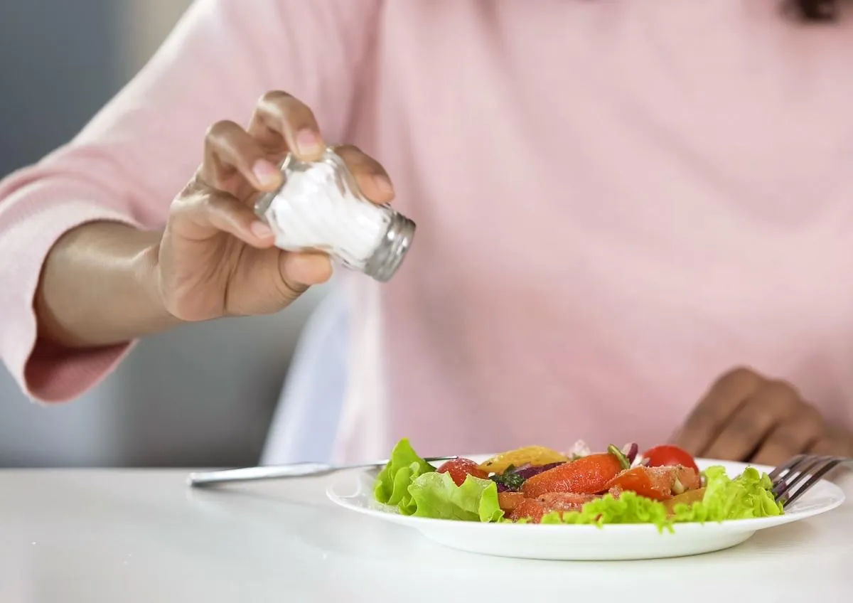 woman adding too much salt to her food, unhealthy eating, dehydration problems