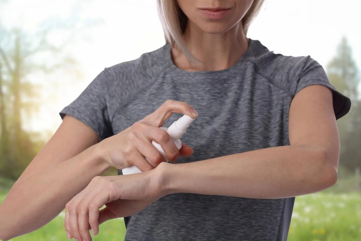 woman spraying insect repellent on skin outdoor